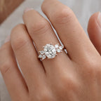 Hand wearing an oval cut diamond engagement ring with side stones on a gold band