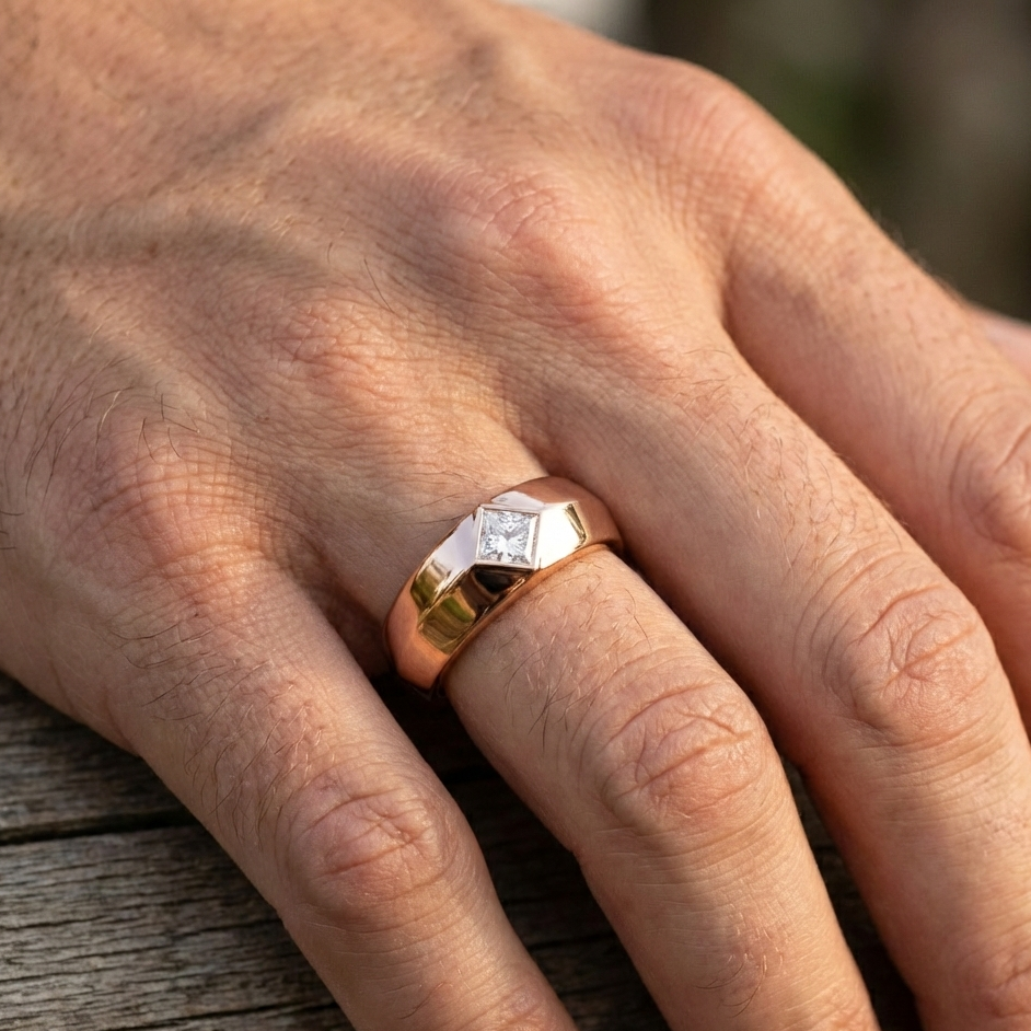 Hand wearing a gold ring with a diamond on a wooden surface