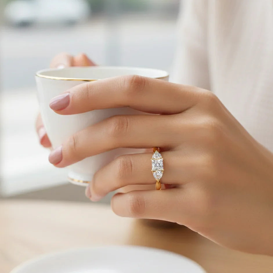 Hand holding a white teacup with a diamond ring on a blurred background