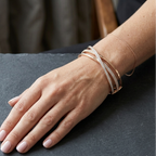 Hand wearing multiple rose gold bracelets on a dark surface