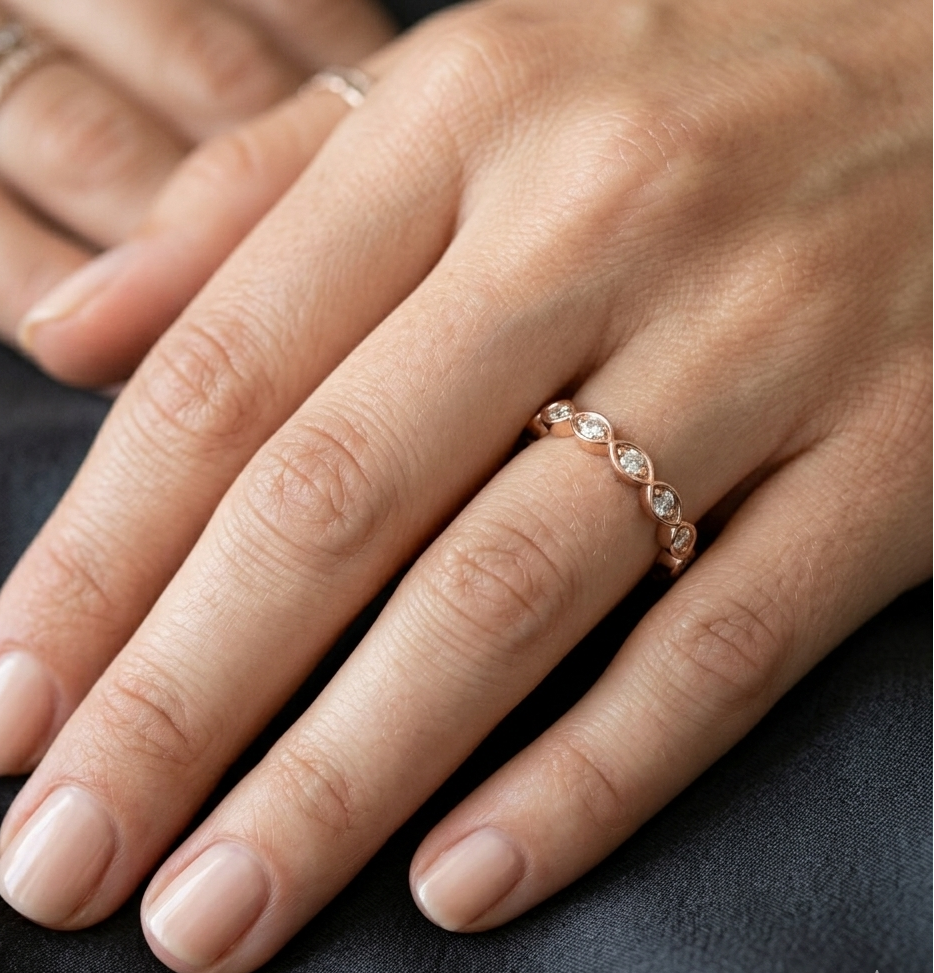 Close-up of a hand wearing a rose gold ring with diamonds on a dark fabric background