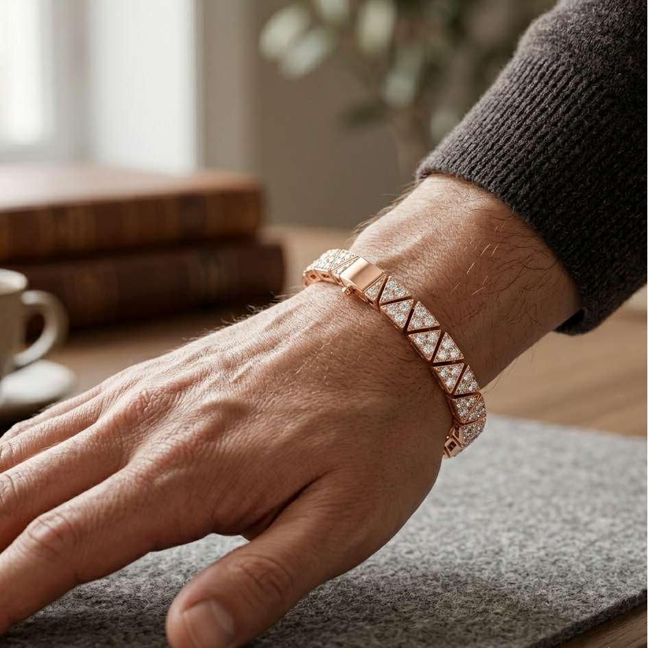 Hand wearing a rose gold bracelet on a wooden surface with books and a cup in the background